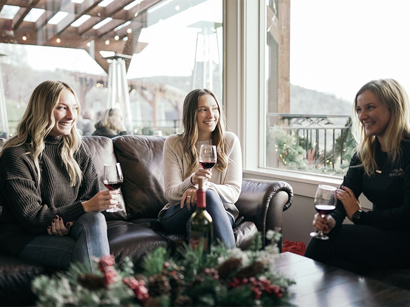 Three women sitting on a couch indoor while enjoying glasses of wine at Tipsy Canyon Winery