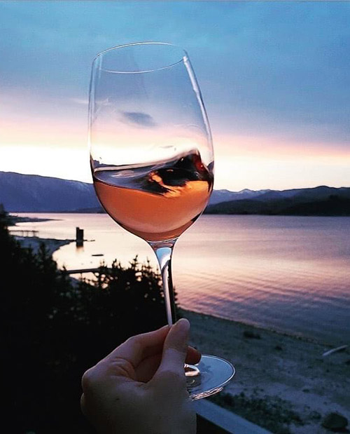 hand swirling rose wine at sunset with lake in background