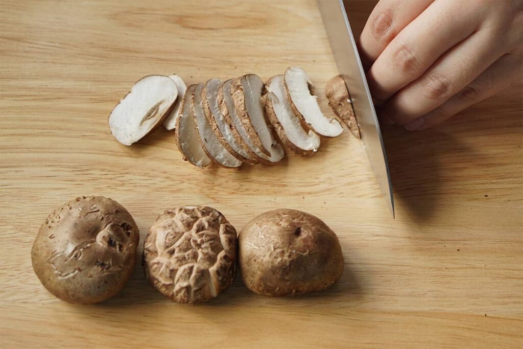 A person's hand chopping and preparing shiitake mushrooms for a wine and food pairing recipe